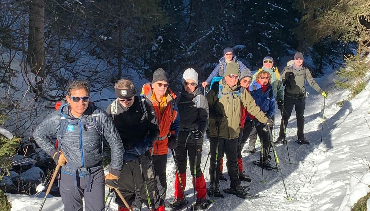 Eine Gruppe Schneeschuwanderer steht vor dem Wald und lässt sich von der Sonne bescheinen | © DAV Flensburg