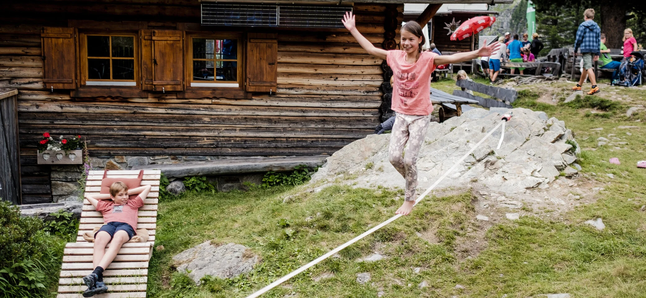 Zwei Kinder balancieren auf einem Seil, das vor einer Berghütte gespannt ist | © DAV/Hans Herbig